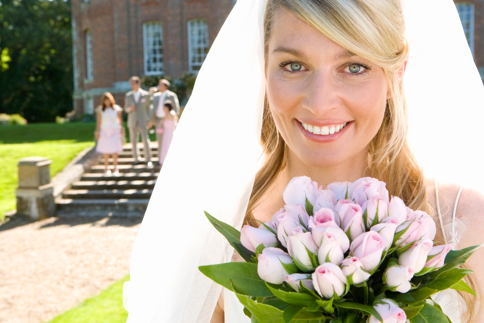 A bride with pink tulips smiles outside a brick building in Cooper City, near med spas, with three people in the background.
