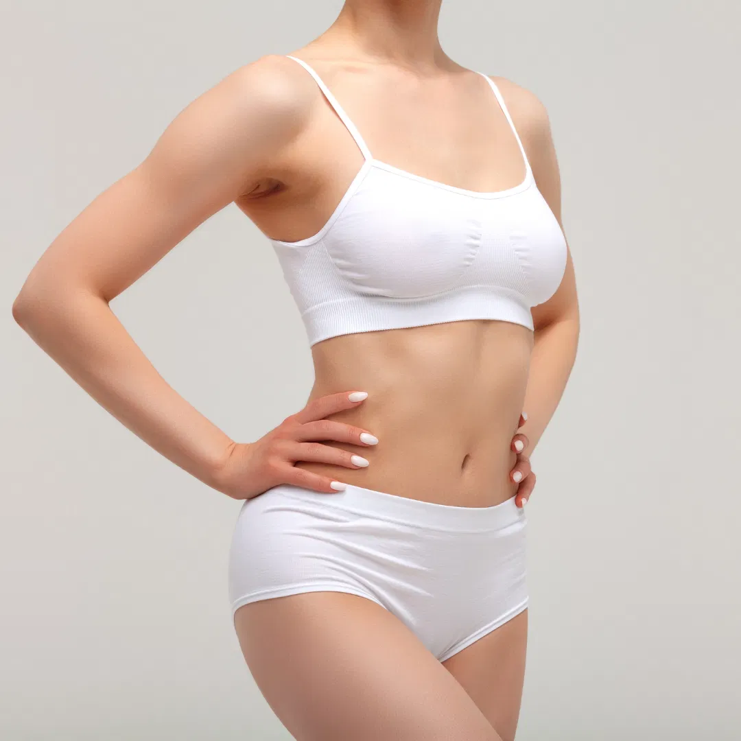 Woman wearing a white bra and underwear set stands with hands on hips against a plain, light background, representing the confidence and wellness associated with med spas in Cooper City. Her face is not visible.