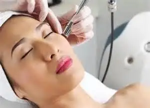 Person with closed eyes receiving a facial treatment using a handheld device at a med spa in Cooper City, while wearing a towel headband. A gloved hand is holding the device near the person’s cheek.
